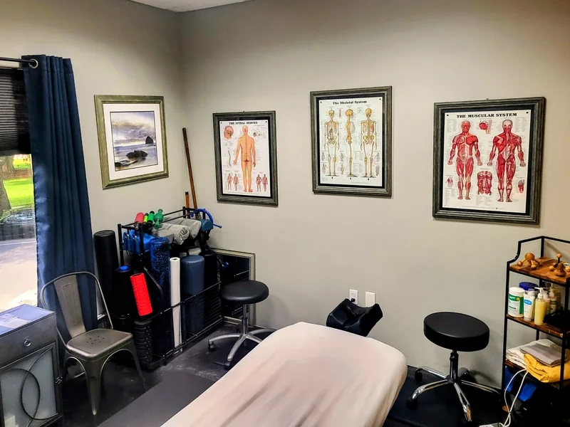 The treatment room at Windows of Wellness in Lake Mary, FL — massage table, anatomy charts, mobility equipment and daylight from the street window